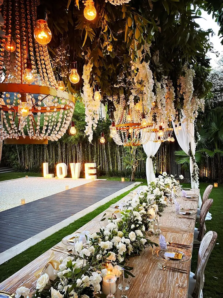 A long wedding table under hanging flowers and lights