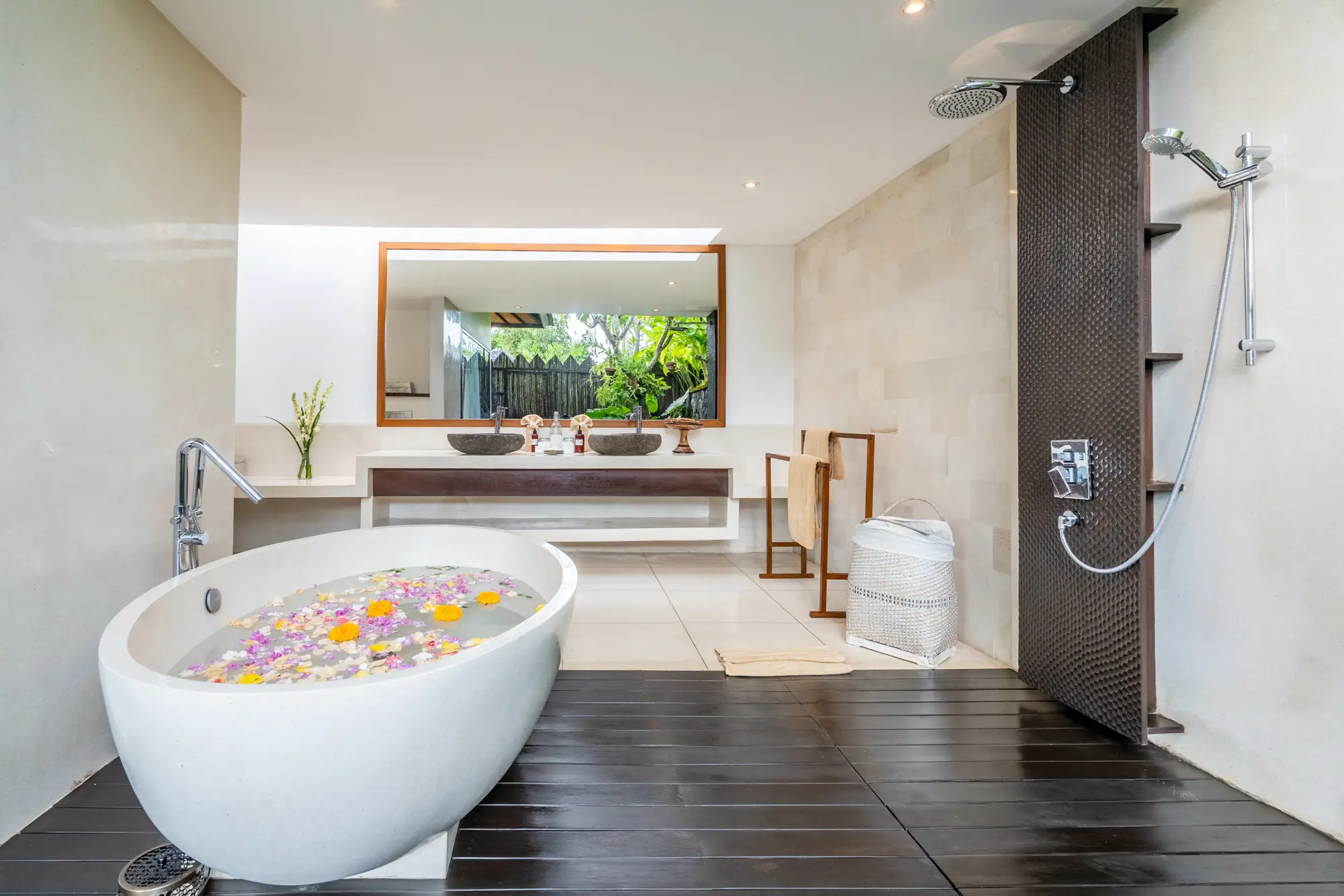 A freestanding bathtub with flower petals beside a garden window