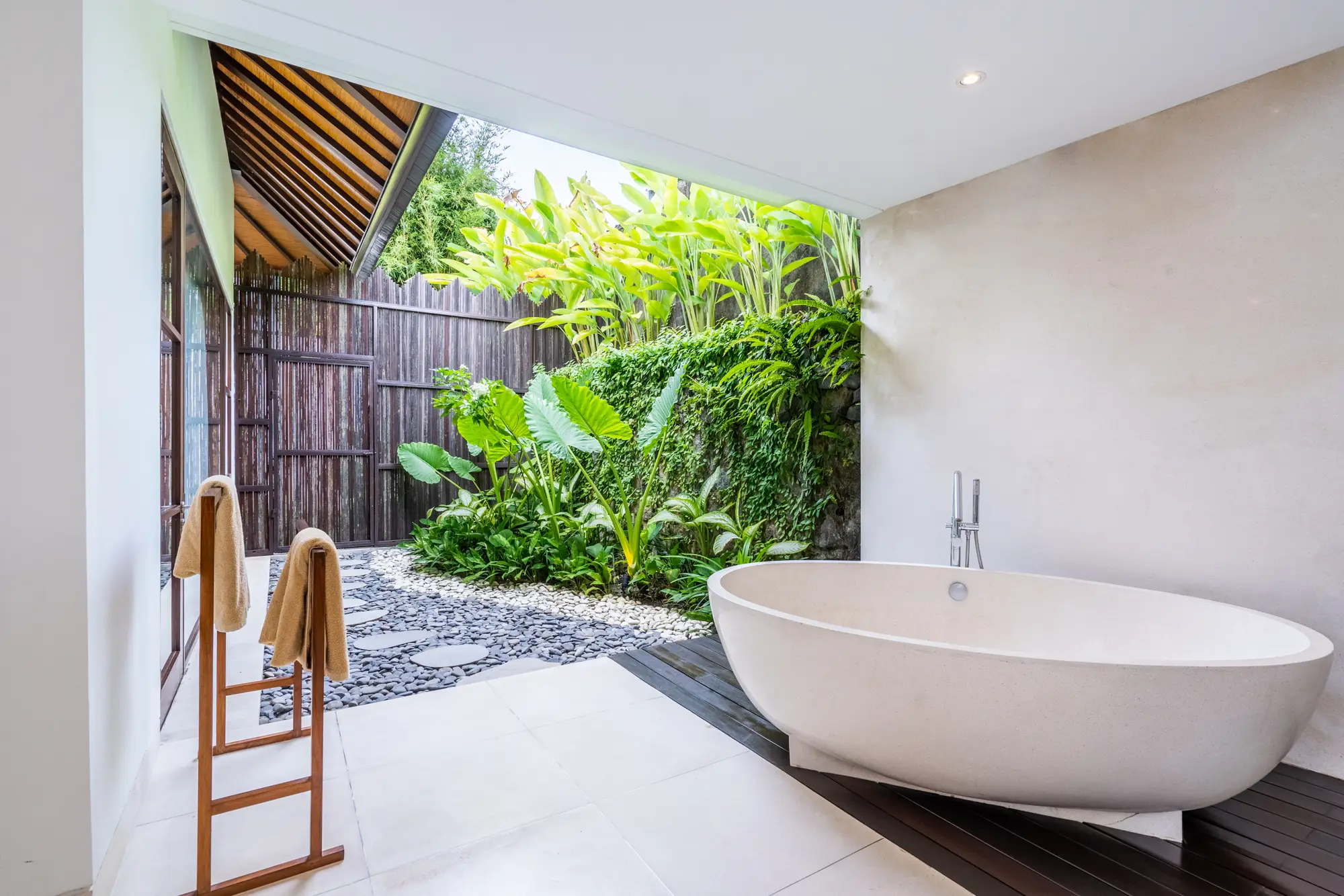 An outdoor bathroom with a freestanding tub among plants