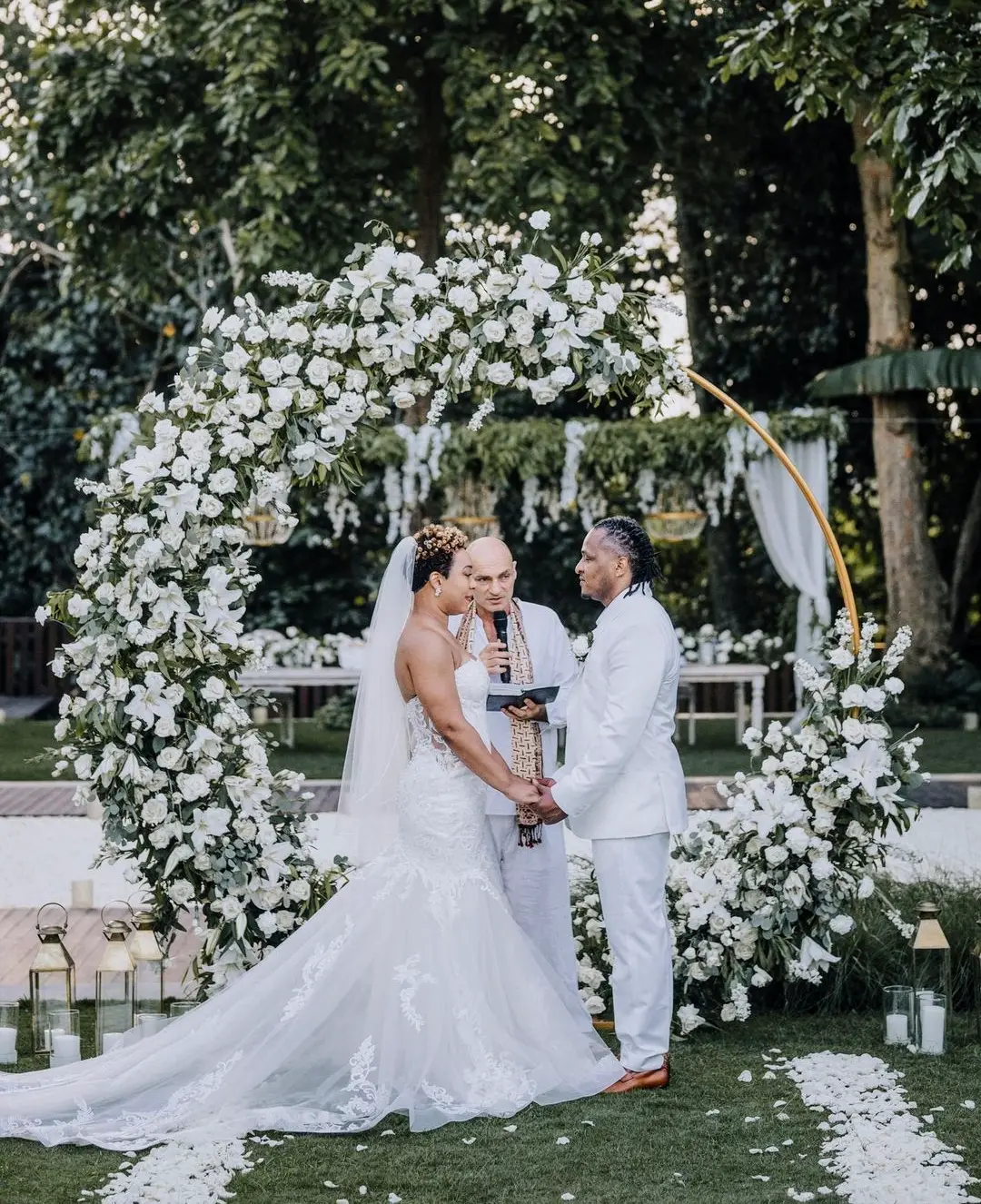 A bride and groom under a white floral arch