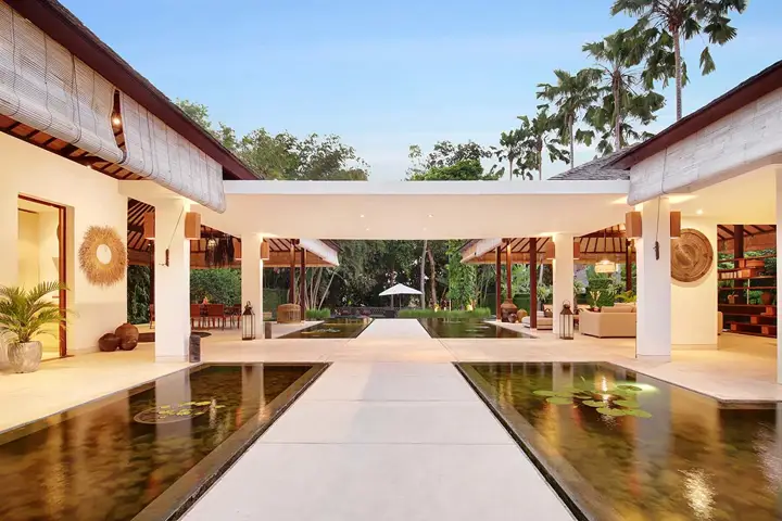 A white walkway between two reflecting ponds, leading through the villa