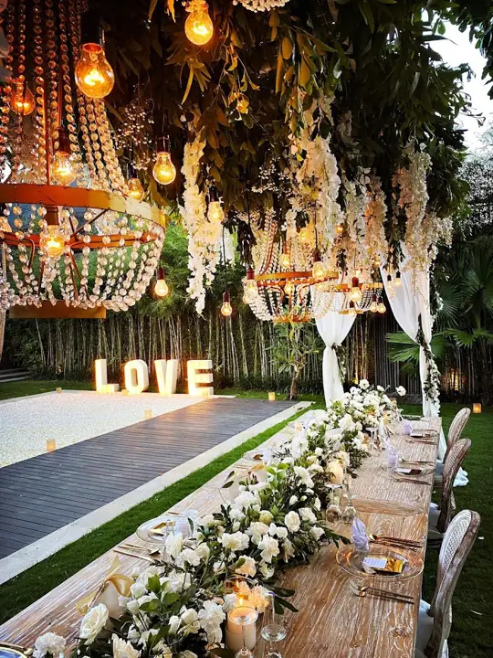 A long wedding table under hanging flowers and lights
