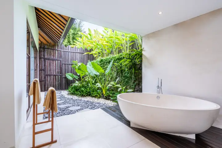 An outdoor bathroom with a freestanding tub among plants