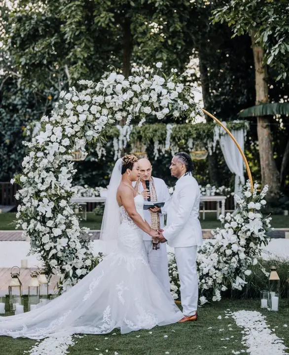 A bride and groom under a white floral arch