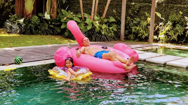 A father and daughter floating on a pink flamingo in the pool